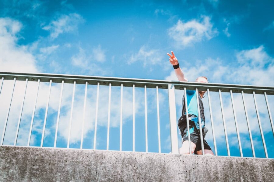 Läufer zeigt Peace-Zeichen auf einer Brücke